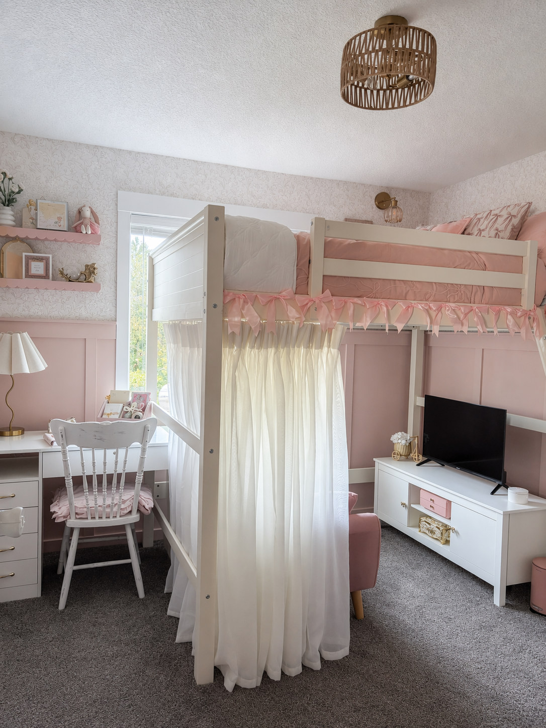 A high-quality, cozy girls' bedroom featuring a white loft bed with a pink ruffled canopy and sheer white curtains, set against soft pink paneled walls — loft bedroom ideas reference 3