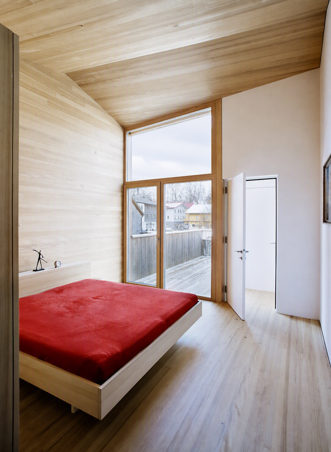 Modern minimalist bedroom with light wood ceiling, walls, and flooring, featuring a floating bed with a vibrant red mattress — minimalist bedroom ideas reference 1