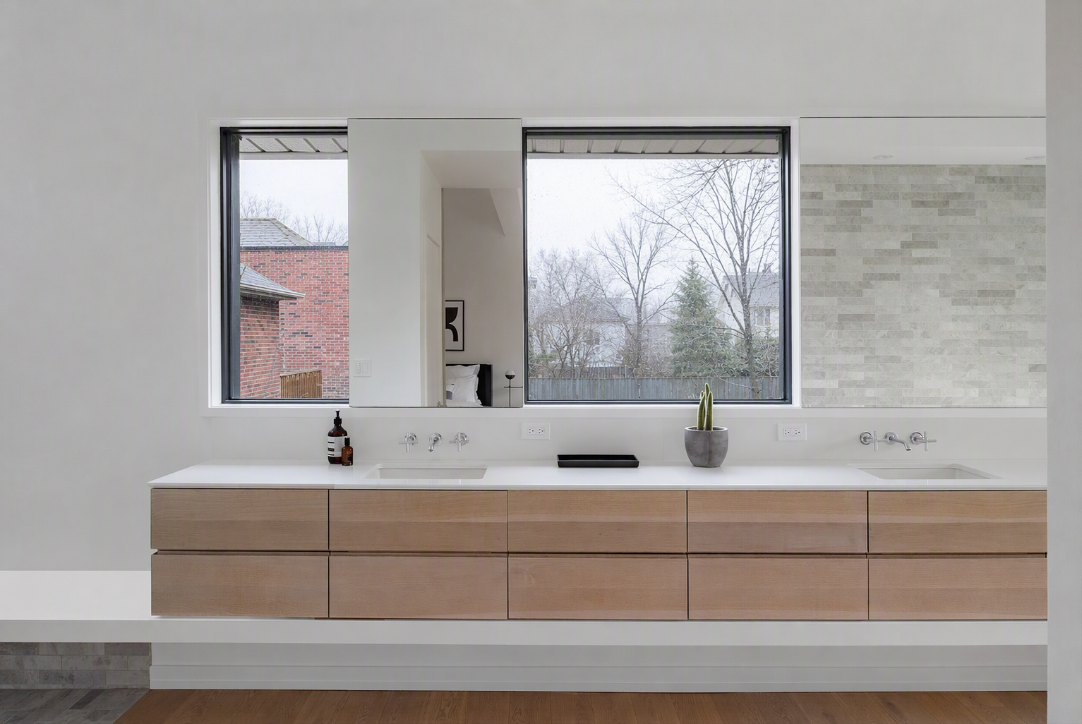Modern minimalist bathroom with a long white countertop featuring two built-in sinks, light wood cabinetry below, and large black-framed windows offering — bathroom backsplash ideas reference 1